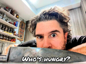 Man raising one eyebrow behind an upside down knife with the words "Who's Hungry" on it.