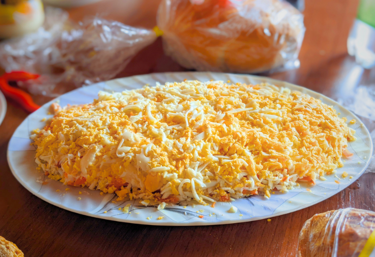 Herring Under a Blanket - layered herring salad with shredded eggs on top, served on a white platt.