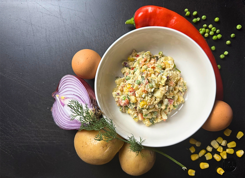 Traditional Polish vegetable salad (Sałatka Jarzynowa) in a white bowl, made with potatoes, carrots, peas, eggs, pickles, and mayonnaise, surrounded by fresh ingredients on a dark background.